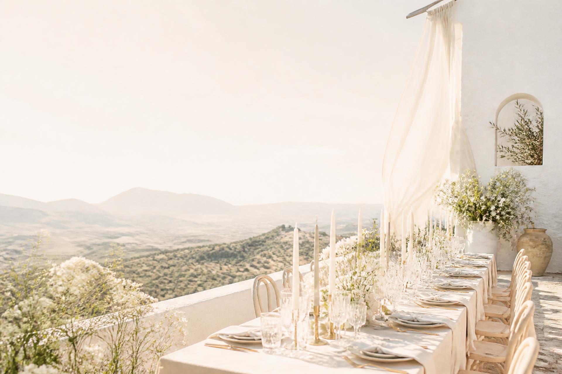 Sun-drenched Mediterranean terrace set for a wedding dinner, olive hills beyond